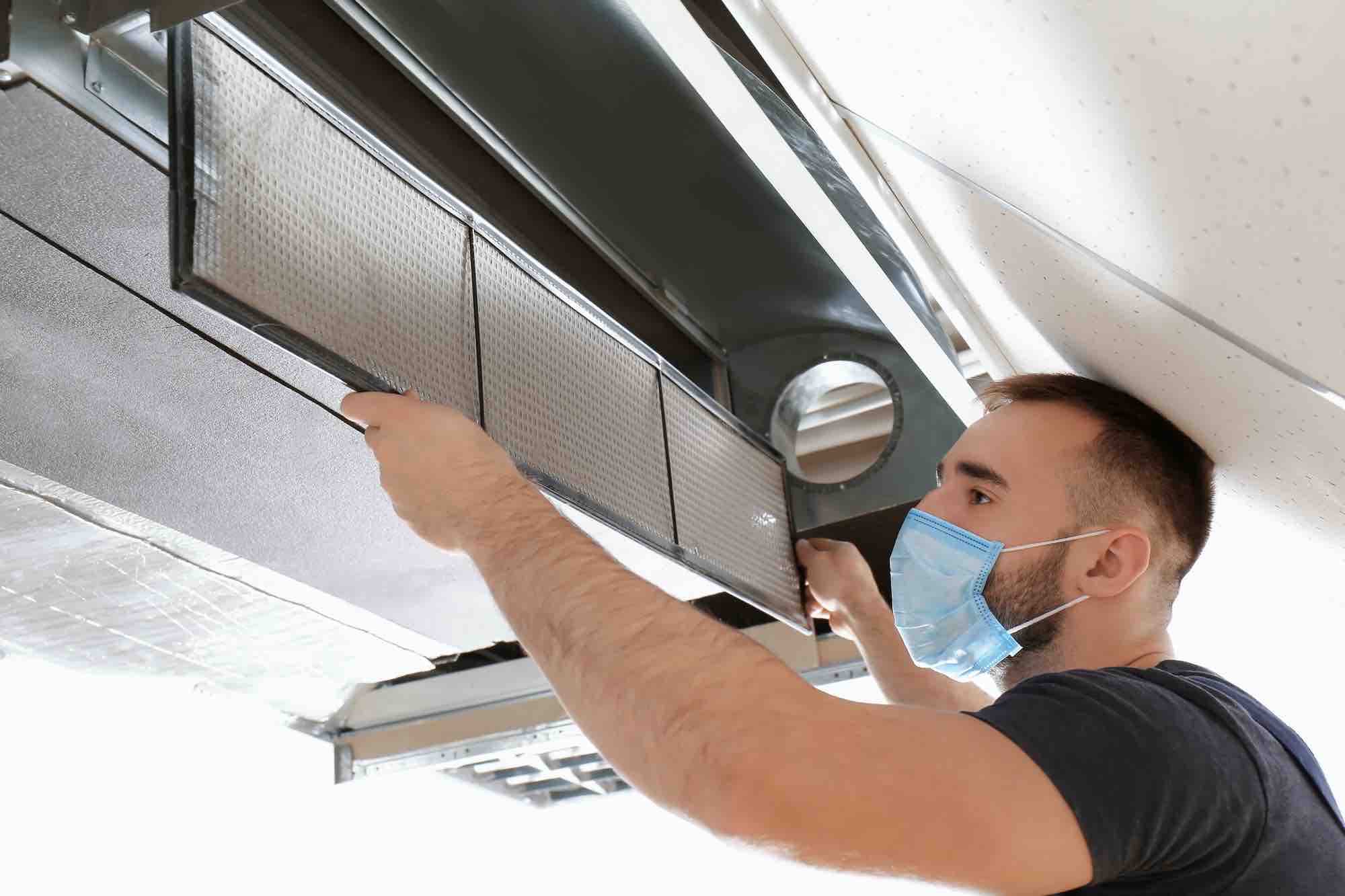 Male technician cleaning industrial air conditioner indoors